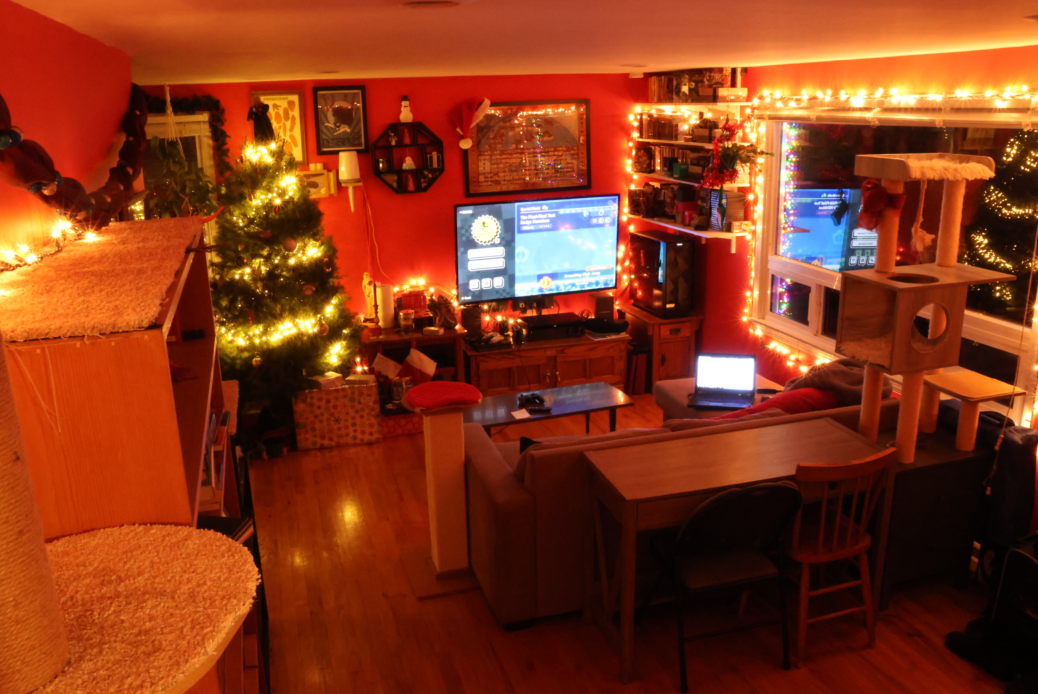 Living room in 2023. It's dark this year, as these photos were taken late in the day, but is otherwise largely unchanged from last year! A few more things on the walls, a few more bits of cat furniture. The dark makes the warm glow of the christmas lights particularly pleasant.