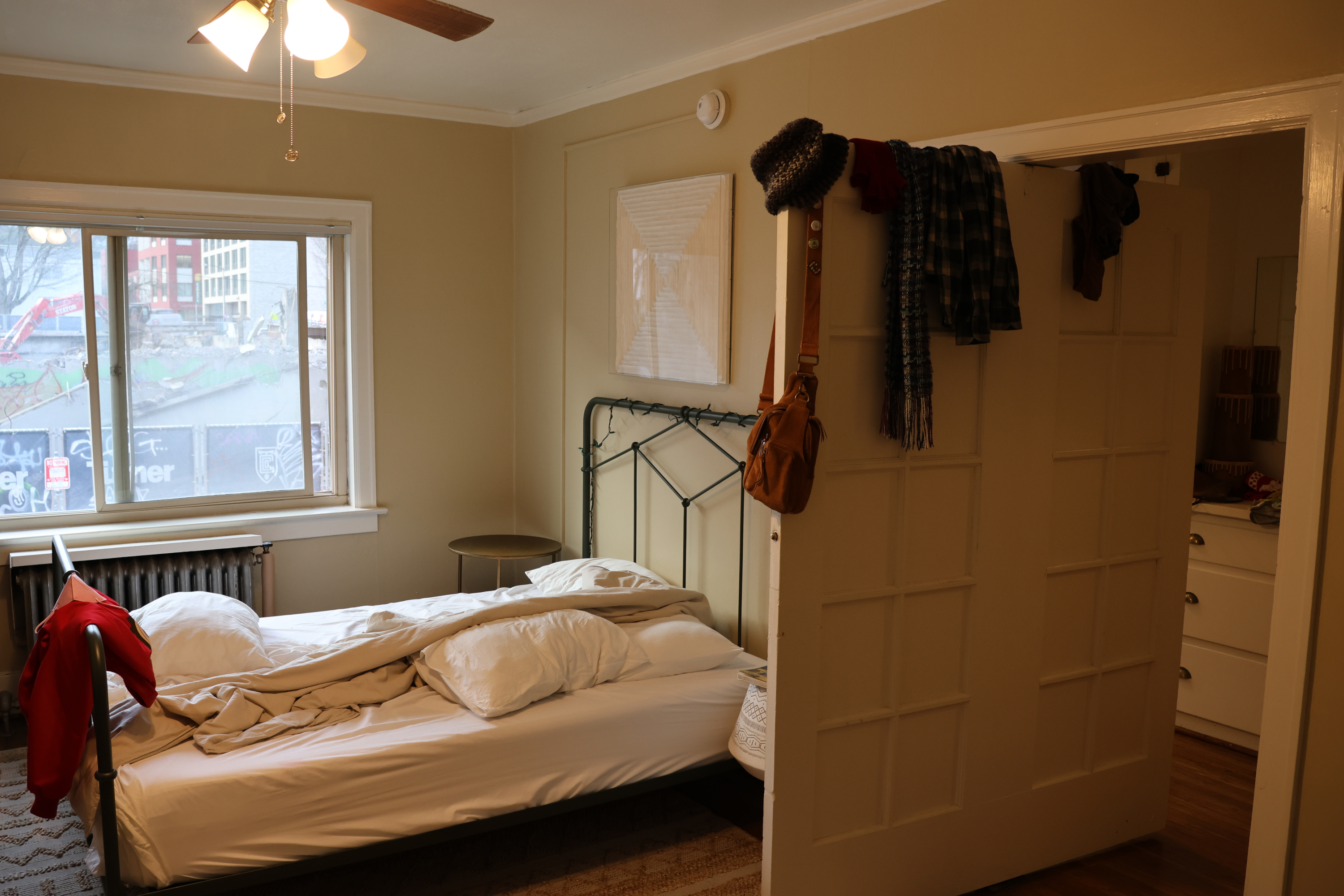 Photo of a small apartment. In frame is a slept-in bed, and a double-width door which rotates around a pivot at its center. We've got it fully open now, and our clothes are hanging on it.