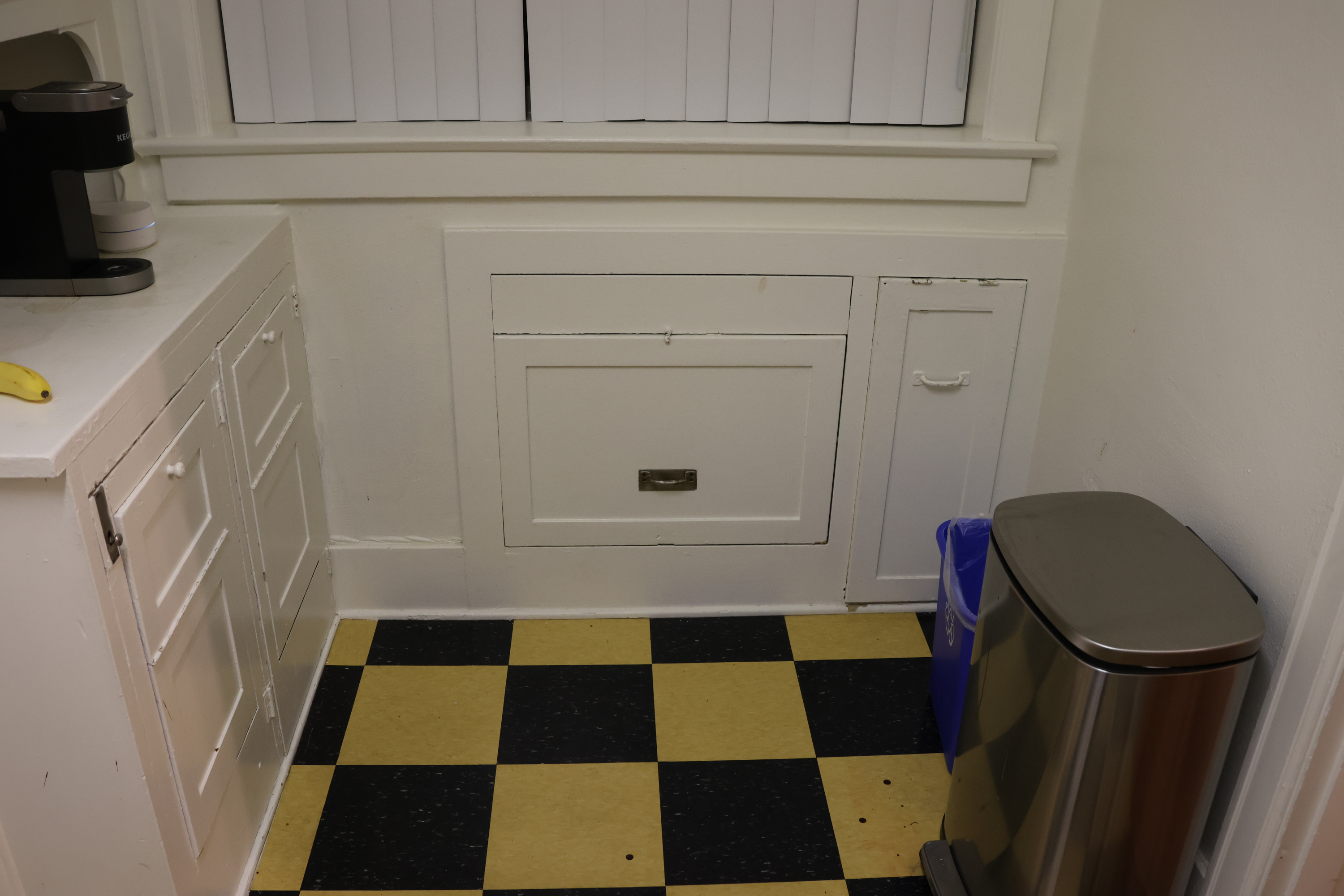 A nook in the kitchen with odd cabinetry built into the walls. Particularly odd are a tall narrow door on the right, and a large square cabinet in the center.