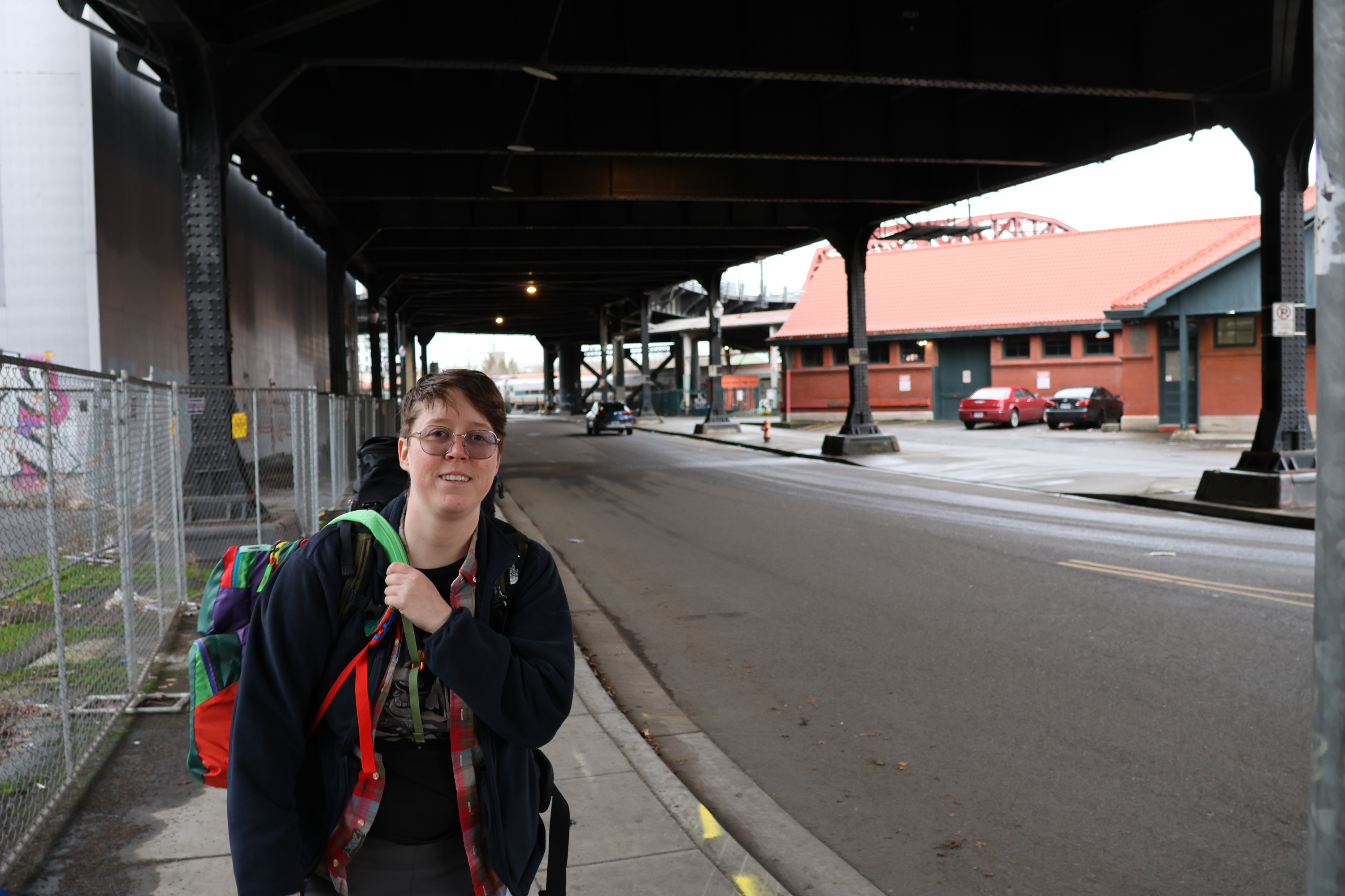 Morrie in the left third of frame. It's not too cold today so she's able to wear her coat open, but she's laden down with two backpacks. We're walking under an overpass.